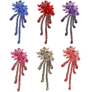 Peut inclure: Six écussons floraux brodés de différentes couleurs : bleu, rouge, violet, rose, beige et corail. Chaque écusson présente un bouquet de fleurs avec de longues extensions pointues en forme de plumes. Les écussons sont sur fond blanc.