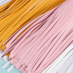 Pu&ograve; includere: Primo piano di una frangia multicolore con fili gialli, rosa e bianchi. La frangia &egrave; in pelle e probabilmente viene utilizzata a scopo decorativo.