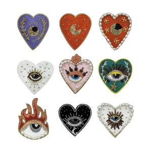 May include: Nine embroidered heart-shaped patches with various designs. Some feature an eye with eyelashes, others have a crescent moon and stars, and one has a flame design.