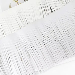 Pu&ograve; includere: Frange bianca con una frangia lunga e sottile. La frangia &egrave; realizzata in un materiale morbido e flessibile, perfetta per aggiungere un tocco di texture e movimento a qualsiasi progetto.