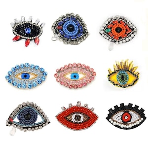 Puede incluir: Nueve amuletos de ojo turco diferentes con varios colores y diseños. Los amuletos están hechos de cuentas y pedrería. Los amuletos tienen todos la forma de un ojo.