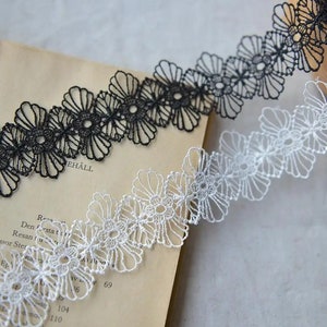 May include: Two pieces of delicate lace trim with a floral design. One piece is black and the other is white.