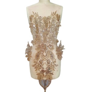 Könnte beinhalten: Goldene Perlenapplikation mit floralem Muster. Die Applikation ist auf einem Netzrücken und eignet sich perfekt zum Verzieren von Kleidung oder Bastelarbeiten.