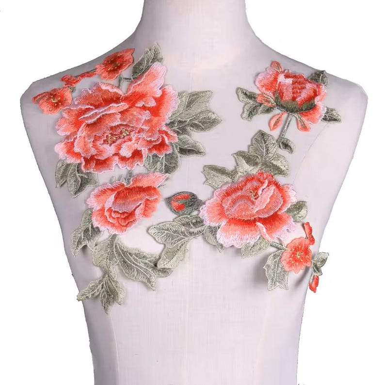 May include: A delicate floral applique featuring pink and green embroidered flowers. The applique is perfect for adding a touch of elegance to clothing, accessories, or home decor projects.