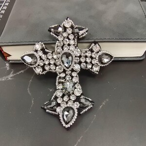 Può includere: Un ricamo a forma di croce nero e argento con strass trasparenti e grigio scuro.