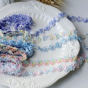 Op de afbeelding: Assortiment van pastelkleurige bloemenkant. De kant heeft een delicaat madeliefje-ontwerp in tinten blauw, roze en geel.