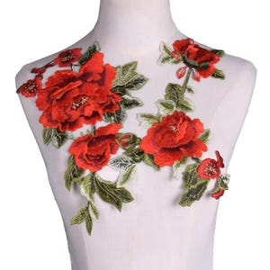 May include: Red floral applique with green leaves. This embroidered patch features a delicate design with multiple red roses and green leaves.
