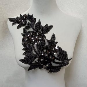 Puede incluir: Aplique floral negro con lentejuelas y cuentas. El aplique presenta un diseño de hojas y flores.