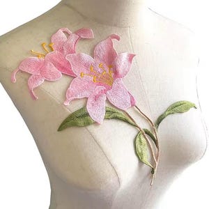 May include: Pink embroidered lily flower applique with green leaves. This floral applique is perfect for adding a touch of elegance to clothing, bags, or home decor projects.