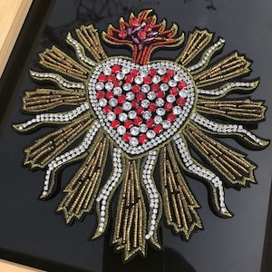 May include: A red heart with gold and white beads, surrounded by a halo of gold and white beads. The heart is embellished with red and clear rhinestones.