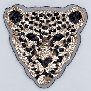 Op de afbeelding: Een luipaardkop-patch gemaakt van glinsterende gouden en zwarte lovertjes op een transparante zwarte mesh-ondergrond. Het ontwerp toont een gedetailleerd katachtig gezicht met puntige oren, gedefinieerde ogen en een neus.