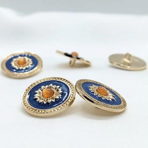 May include: Four gold-toned buttons with a blue enamel finish and a raised orange centre. The buttons have a decorative gold border.