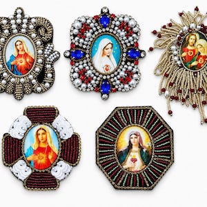 May include: Five decorative brooches featuring religious imagery. Each piece is embellished with intricate beadwork, pearls, and crystals surrounding central oval portraits of religious figures in vibrant colors against a plain white background.