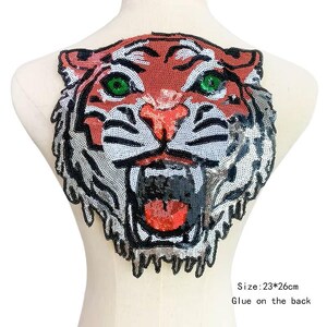 May include: A red, white, and black tiger face applique with green eyes. The applique is made of sequins and is approximately 9.06 inches by 10.24 inches. The text "Size: 23*26cm Glue on the back" is printed below the applique.