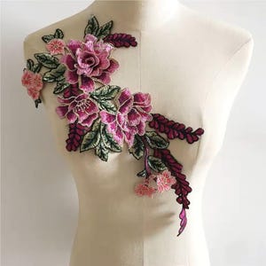 May include: A pink and green floral applique with a large pink flower in the centre. The applique is ideal for adding a touch of elegance to clothing, bags, or home decor.