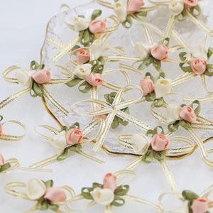 May include: A collection of delicate, handmade bows with pink and white satin ribbon flowers. The bows are tied with gold ribbon and are perfect for adding a touch of elegance to any project.