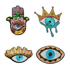 May include: Four decorative patches with eye and hand designs. The patches feature sequins in various colors, including blue, gold, pink, and green. One patch is a Hamsa hand, and another is a crown with an eye.
