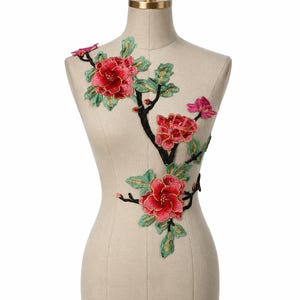 Peut inclure: Applique florale brodée avec des fleurs rouges vives, des accents dorés et des feuilles vertes. Le motif comprend une branche noire et est présenté sur un mannequin, pour la mode ou l'artisanat.