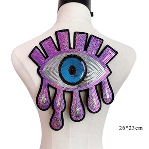 Può includere: Toppa a forma di occhio in paillettes viola e blu con un design a forma di lacrima. La toppa misura 26 cm per 23 cm.