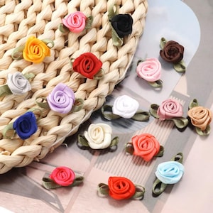 Puede incluir: Surtido de pequeñas decoraciones de rosas de tela en varios colores, incluyendo rosa, rojo, azul, blanco y amarillo. Las rosas están dispuestas sobre un fondo de cesta tejida.