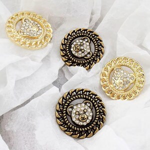 May include: Four gold-tone and bronze-tone metal buttons with a rhinestone bear design. The buttons have a chain-link border.