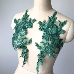 May include: Two green floral lace appliques with sequins. The appliques are on a white background and are perfect for adding a touch of elegance to any project.