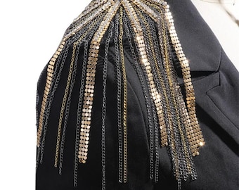 May include: A black blazer with a gold and silver chain shoulder embellishment. The chains are made of small, linked squares and hang down from the shoulder in a cascade.