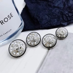 Puede incluir: Tres botones plateados con un dise&ntilde;o de perlas y diamantes de imitaci&oacute;n. Los botones son redondos y tienen un centro elevado con un patr&oacute;n decorativo.