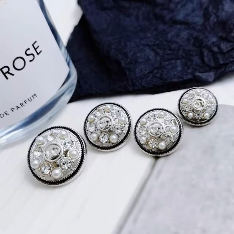 Puede incluir: Tres botones plateados con un dise&ntilde;o de perlas y diamantes de imitaci&oacute;n. Los botones son redondos y tienen un centro elevado con un patr&oacute;n decorativo.