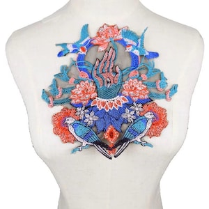 May include: Embroidered applique patch featuring a hand with stylized flowers and birds in shades of blue, pink, and orange. The patch is on a sheer mesh background.