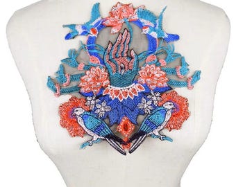 May include: Embroidered applique patch featuring a hand with stylized flowers and birds in shades of blue, pink, and orange. The patch is on a sheer mesh background.