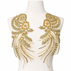 May include: A pair of symmetrical gold sequin and bead embroidered appliques featuring floral and swirling leaf motifs. The decorative pieces are crafted with metallic gold thread, shimmering sequins, and small beads arranged in intricate patterns.