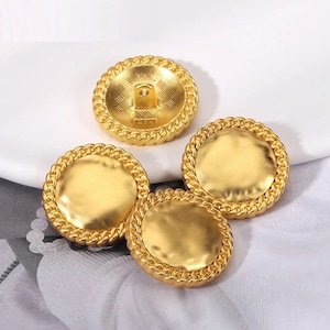 Puede incluir: Tres botones redondos de color dorado con una superficie texturizada y un borde de cuerda. Los botones tienen un agujero en el centro para coser.