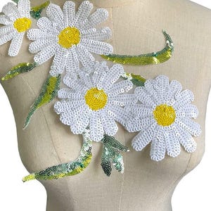 May include: White daisy flower applique with green leaves and yellow centres. The applique is made of sequins and is perfect for adding a touch of whimsy to clothing or crafts.