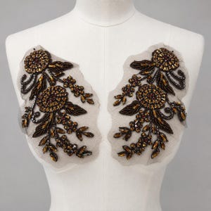 May include: A pair of symmetrical floral appliques featuring dark bronze and amber-colored beads, sequins, and crystals arranged in circular flower and leaf patterns on a sheer, light-colored mesh fabric backing for garment embellishment.