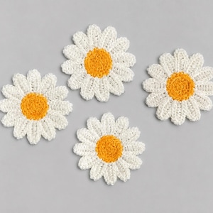 Pode incluir: Um conjunto de quatro bases para copos em croché com formato de margarida, cada uma com um centro circular amarelo brilhante rodeado por pétalas brancas. As bases florais apresentam um acabamento em fio texturizado com pétalas brancas que irradiam do centro.