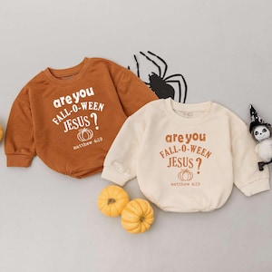 May include: Two baby bodysuits, one in rust and the other in cream, each with the text "are you FALL-O-WEEN JESUS?" and "matthew 4:19". The image includes small pumpkins and a Halloween decoration.
