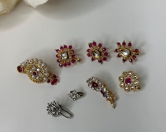 May include: A set of seven gold and silver nose rings with pink and white gemstones. The nose rings are in various shapes and sizes, including a round shape, a square shape, and a flower shape.