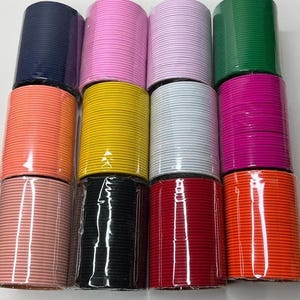 May include: A collection of colorful elastic bands in various shades, including pink, green, orange, yellow, and red. The bands are neatly stacked in cylindrical rolls, offering a vibrant display of colors. These elastic bands are suitable for crafting and sewing projects.