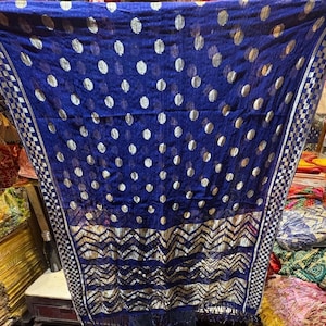 Puede incluir: Una bufanda azul transparente con un patr&oacute;n de lunares plateados y un borde geom&eacute;trico plateado. La bufanda tiene flecos en el borde inferior.