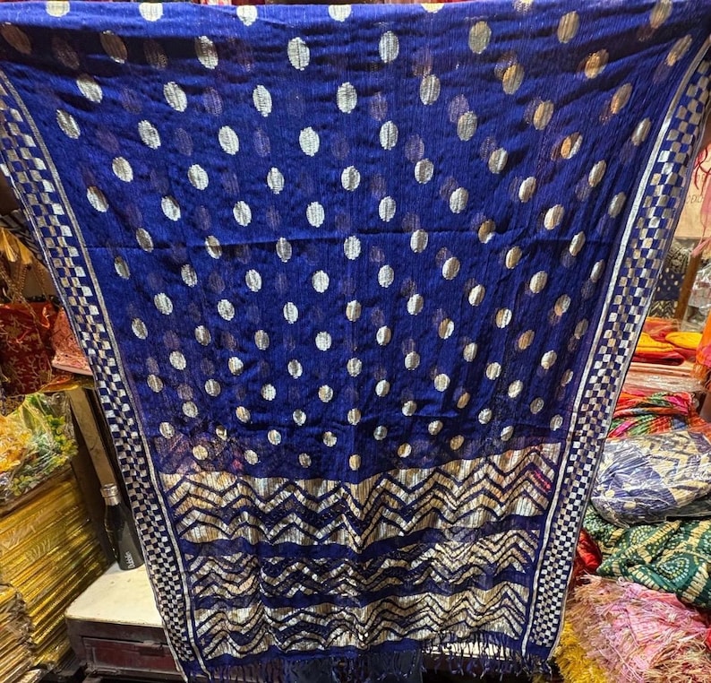 Puede incluir: Una bufanda azul transparente con un patr&oacute;n de lunares plateados y un borde geom&eacute;trico plateado. La bufanda tiene flecos en el borde inferior.