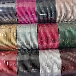 May include: Rows of colorful bangles in various shades, including black, pink, silver, and gold. The bangles are neatly stacked, showcasing a variety of colors and textures. The image highlights the diversity of the jewelry.