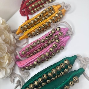 May include: Set of five ankle bells, each with a different color fabric: red, yellow, pink, green, and blue. The bells are made of metal and are attached to the fabric with a string. The bells are used for dancing and other performances.