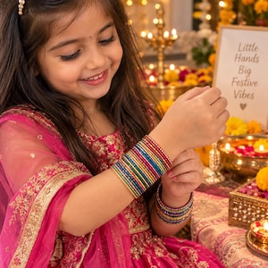 May include: A stack of thin, multicolored metal bangles worn on the wrist, featuring vibrant shades of red, blue, green, and gold. The bangles have a textured, glittery finish. The wearer is dressed in a bright pink garment with gold embroidery.