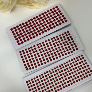May include: Three sheets of red dot stickers. Each sheet has a grid of small, round, red stickers.