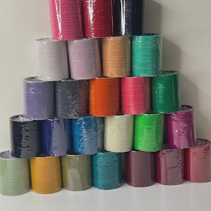 May include: A pyramid of colorful bangles in various shades, including pink, red, navy, and green. The bangles are wrapped in clear plastic and stacked on top of each other. The background is a plain white surface.