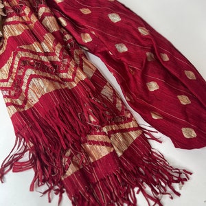 Puede incluir: Una bufanda de color burdeos y dorado con un borde de flecos. La bufanda tiene un patr&oacute;n geom&eacute;trico y un dise&ntilde;o de puntos.