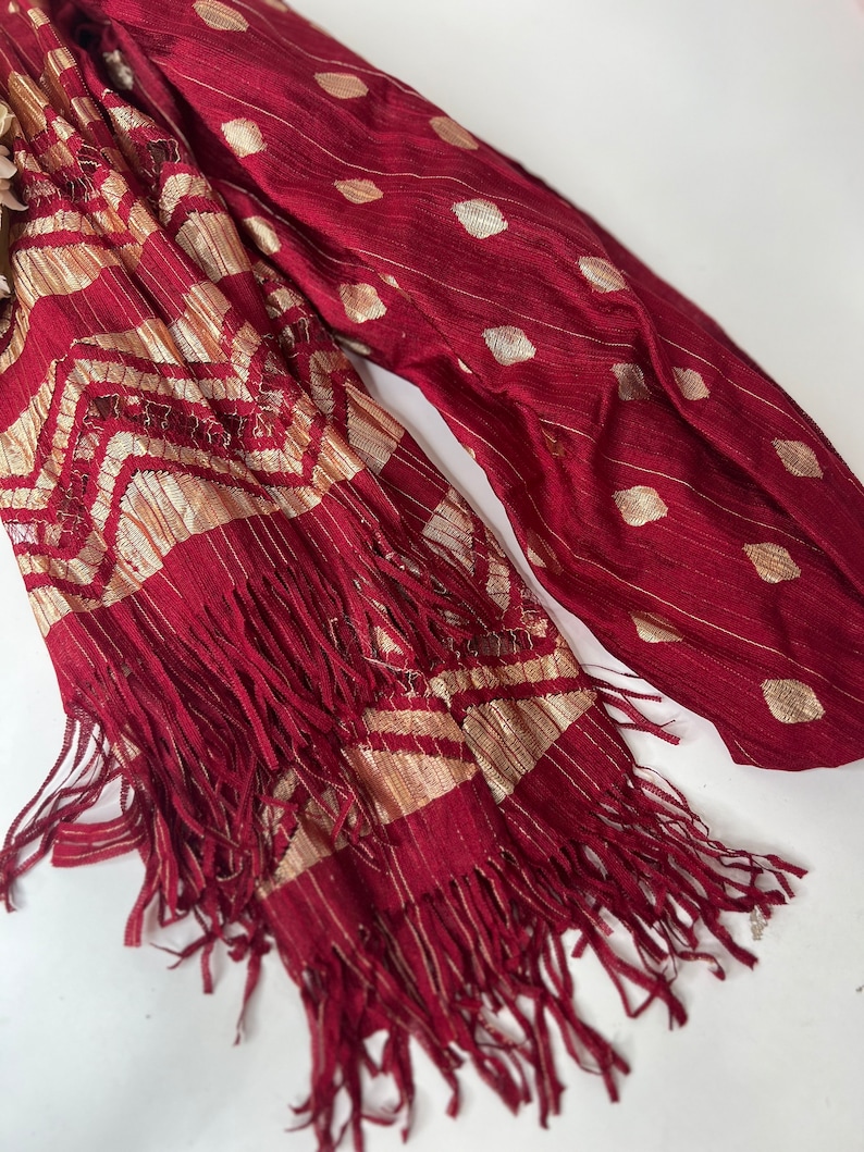 Puede incluir: Una bufanda de color burdeos y dorado con un borde de flecos. La bufanda tiene un patr&oacute;n geom&eacute;trico y un dise&ntilde;o de puntos.