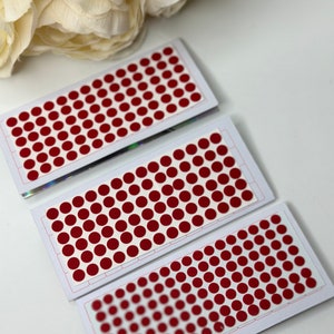 May include: Three sheets of red circle stickers on white cardstock. Each sheet has a grid pattern with rows of red circles.