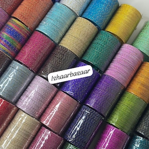 May include: A collection of colorful metal bangles with various patterns and textures. The bangles are stacked and arranged in a display, showcasing a variety of colors and designs. The text "Izhaarbazaar" is visible in the center of the image.